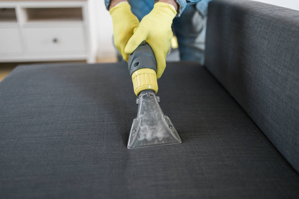 Hombre tintorerías empleado mano en guantes de goma protectora limpieza sofá con método de extracción profesional. Limpieza regular a principios de primavera. Empresa de limpieza comercial - Foto, imagen