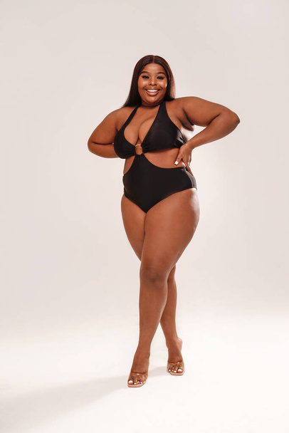 Full length photo Of Curvy Smiling African American Woman posing in black swimsuit. Studio shot. Body positive.  - Photo, Image
