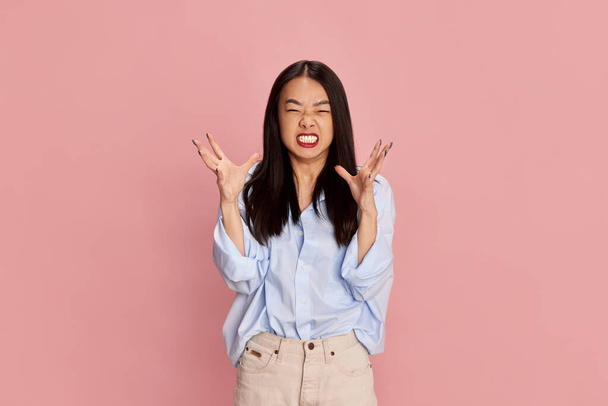Irritation and stress. Portrait of young beautiful girl in casual clothes posing with angry face against pink studio background. Concept of emotions, facial expression, fashion, youth, lifestyle. Ad - Photo, Image
