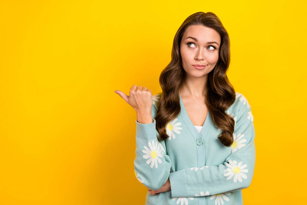 Photo of dreamy uncertain woman wear turquoise cardigan pointing thumb looking empty space isolated yellow color background. - Photo, image