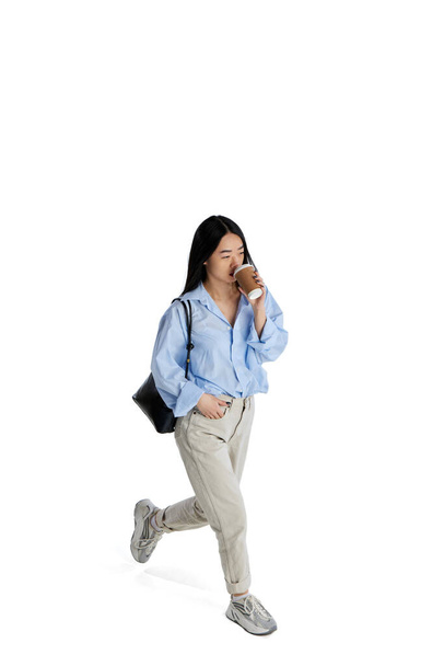 Top isometric view. Young girl in casual clothes in motion, walking and drinking coffee isolated over white studio background. Concept of business, employment, education. lifestyle. Copy space for ad - Фото, изображение