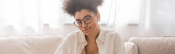 Femme afro-américaine souriante en lunettes regardant la caméra à la maison, bannière  - Photo, image
