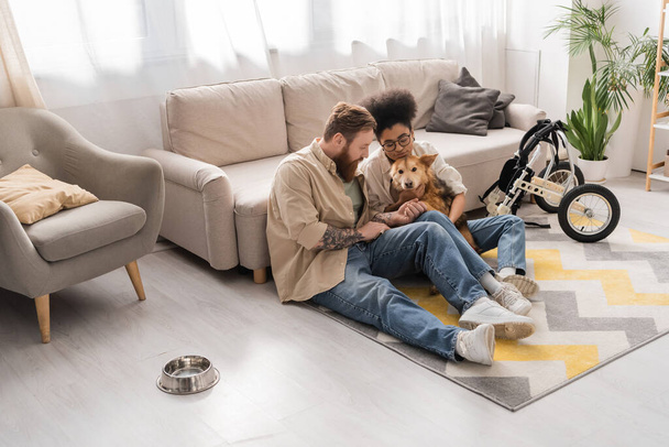 Tattooed man sitting near african american girlfriend and disabled dog in living room  - Foto, imagen