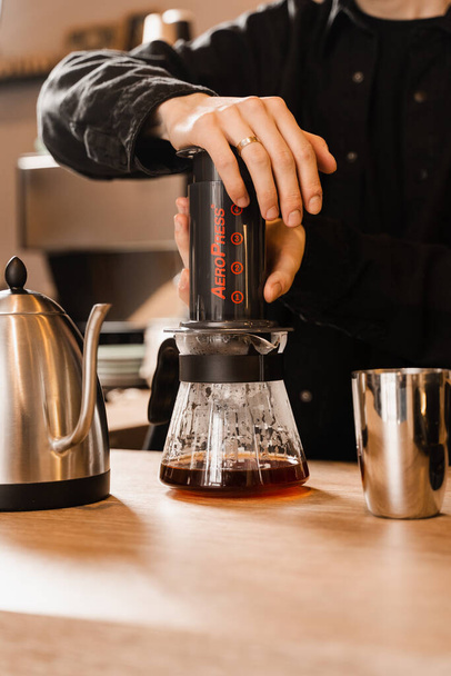 Barista is pushing aeropress for pouring coffee drops trought aeropress to pot. Alternative scandinavian coffee brewing method. Aeropress coffee - Fotó, kép