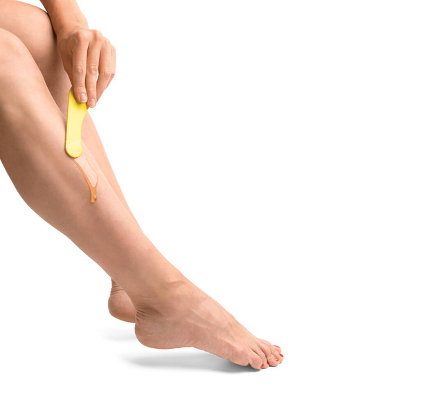 The girl does depilation of the legs in isolation. The girl's hand applies wax for depilation on the leg on a white background. Skin shugaring. Body care. Smooth legs. - Foto, afbeelding