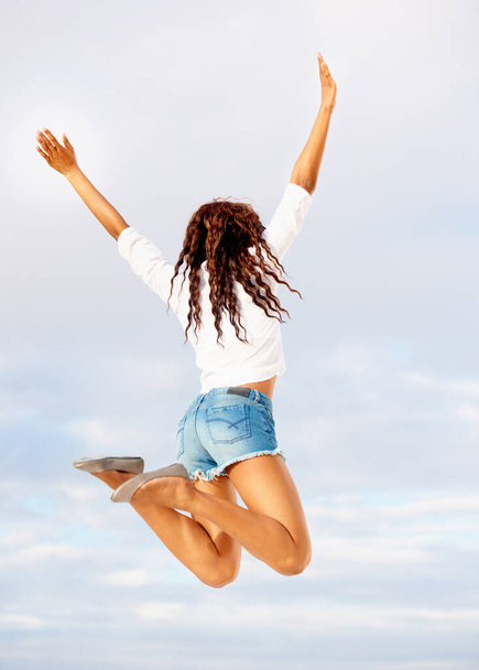 Filled with energy. Happy young woman jumping against a blue sky - Valokuva, kuva