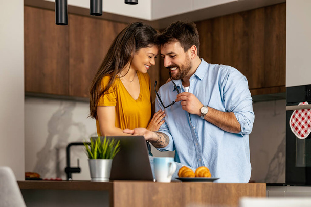 Couple using laptop while drink coffee in their kitchen.Couple in modern kitchen using laptop. - Photo, Image