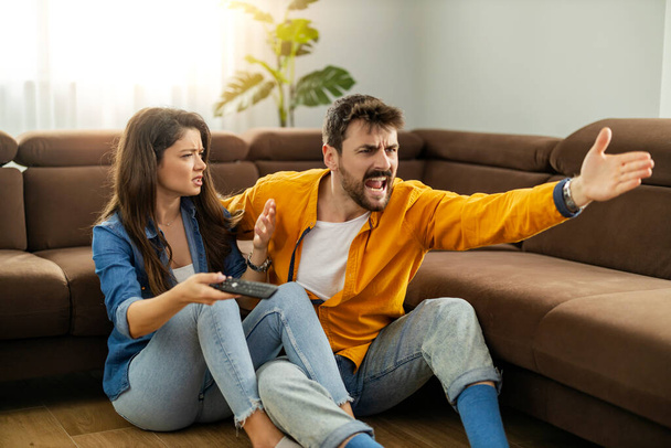 Young couple disappointed while watching sports match on TV at home. - Zdjęcie, obraz