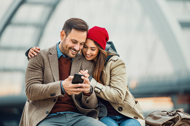 Liebendes junges Paar lächelt zusammen: Sie nutzen Smartphone. - Foto, Bild