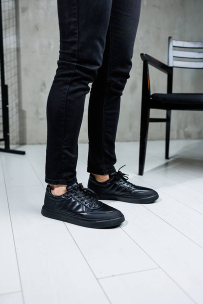 Male legs in black jeans close-up in black leather casual sneakers. Comfortable men's demi-season shoes - Fotoğraf, Görsel