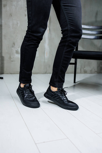 Miespuoliset jalat mustissa farkuissa lähikuva mustissa nahkaisissa rennoissa lenkkareissa. Miesten puolikauden mukavat kengät - Valokuva, kuva