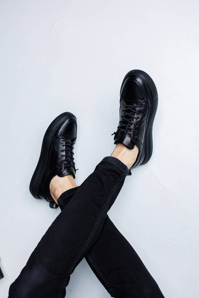 Cierre de piernas masculinas en jeans negros y zapatillas casual de cuero negro. Cómodos zapatos de demi-temporada para hombres - Foto, Imagen