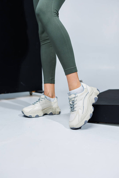 Λεπτά γυναικεία πόδια σε κολάν και λευκά κομψά casual sneakers. Γυναικεία άνετα καλοκαιρινά παπούτσια. - Φωτογραφία, εικόνα