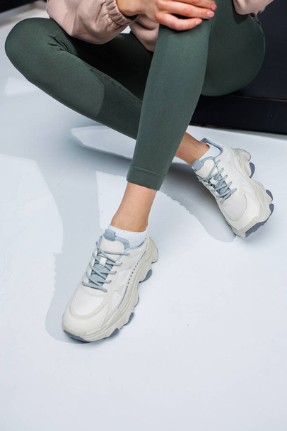Slender female legs in leggings and white stylish casual sneakers. Women's comfortable summer shoes. - Fotografie, Obrázek