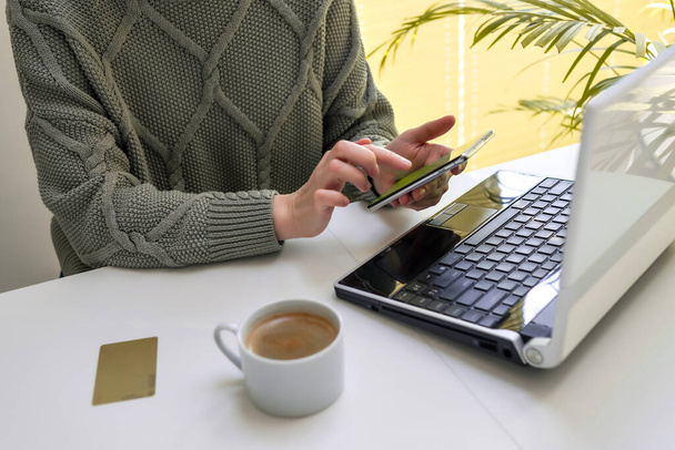 Bir kadın dizüstü bilgisayarda çalışıyor ve telefonunun ekranına bakıyor. Çevrimiçi alışveriş, serbest çalışma, öğrenme, iletişim kavramı - Fotoğraf, Görsel