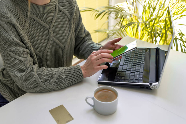 Kobieta pracuje na laptopie i patrzy na ekran swojego telefonu. Koncepcja zakupów online, freelancing, nauka, komunikacja - Zdjęcie, obraz
