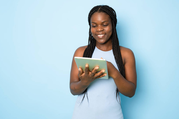 Attractive young African American woman using her high-tech electronic device to help her in education isolated on light blue background - Foto, imagen