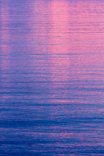 Vivid pink sunset or sunrise reflected on calm blue water in a full frame weather background - Fotografie, Obrázek