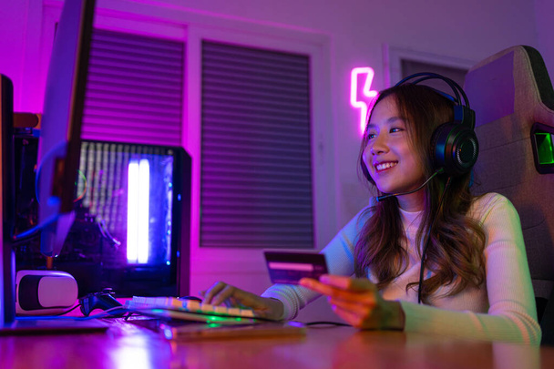 Top up online game with credit card concept. Gamer and E-Sport online of Asian woman playing online computer video game with lighting effect, broadcast streaming live at home. Gamer and E-Sport gaming - Photo, Image