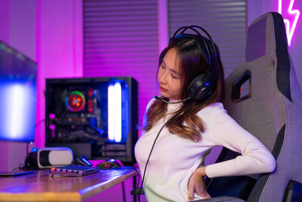 Young people Backache. Gamer and E-Sport online of Asian woman playing online computer video game with lighting effect, broadcast streaming live at home. She a backache due to sitting for a long time - Фото, зображення