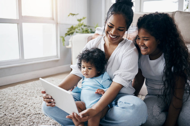 Adora questo show. una giovane donna attraente seduta sul pavimento del soggiorno con i suoi figli e utilizzando un tablet digitale - Foto, immagini