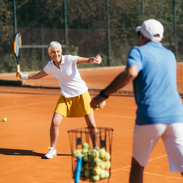 Vanhemmat nainen harjoitellaan Tennis ohjaajan kanssa - Valokuva, kuva