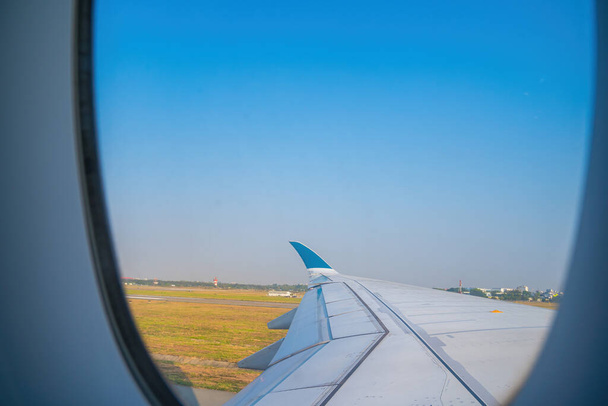 View from airplane window at airport Tan Son Nhat. Blue sky and fluffy white clouds from airplane window view, jet engine on the wing. Booking airline ticket - airplane window seat. Selective focus - Φωτογραφία, εικόνα