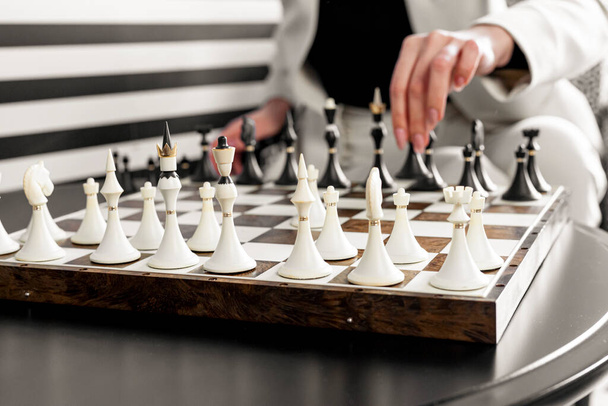 Primer plano de un hermoso tablero de ajedrez con piezas. Una mujer en un estricto traje blanco busca una de las piezas. - Foto, Imagen