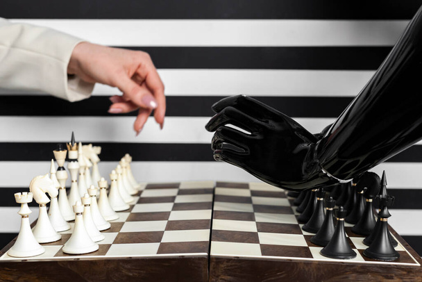Un tablero de ajedrez, una mano femenina humana y una mano robot artificial. Jugar al ajedrez con inteligencia artificial, tecnologías de IA, futuro. - Foto, Imagen