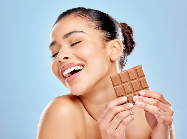 When the cravings just hit too hard. Studio shot of an attractive young woman eating a slab of chocolate against a blue background - Zdjęcie, obraz