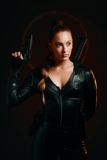 Serious woman, warrior and gun in studio for action, fight and safety from danger on dark background. Strong female assassin or agent in scifi leather cosplay costume with weapon to fight or guard. - 写真・画像