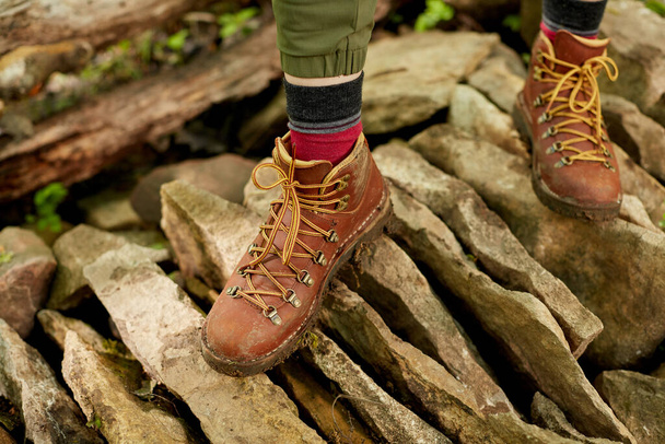 Feet of person in brown hiking boots walking over stones - 写真・画像