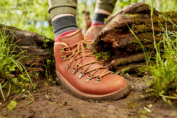 Foot of person in hiking boots stepping over log on forest trail - Foto, imagen