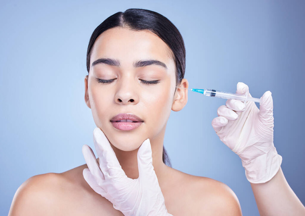 A gorgeous mixed race woman getting botox filler in her face. Hispanic model getting cosmetic surgery against a blue copyspace background. - Valokuva, kuva