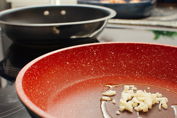 Ail haché frit dans une poêle rouge avec de l'huile d'olive sur une cuisinière à induction - Photo, image