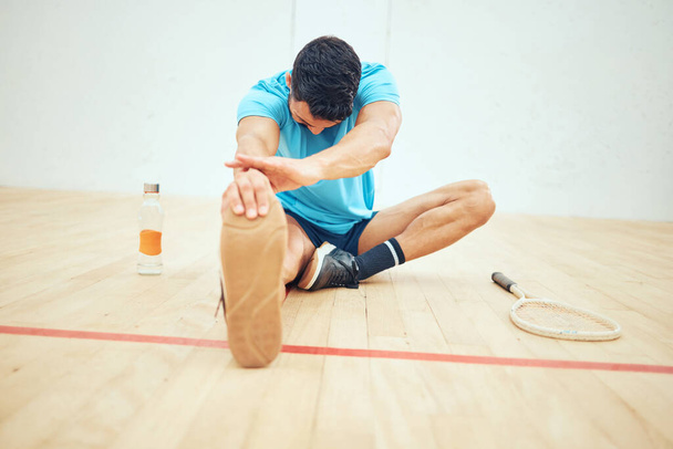 Full length of squash player stretching before playing court game with copyspace. Fit active mixed race athlete sitting alone and getting ready for training practice in sports centre. Sporty hispanic. - Fotoğraf, Görsel