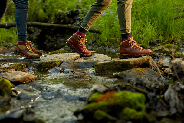 Woman hiker crossing a small forest stream in a close up low angle view of her feet in leather boots on natural rock stepping stones - Valokuva, kuva