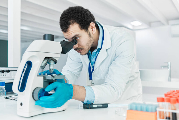 Seguindo processos analíticos cuidadosos. um jovem cientista usando um microscópio em um laboratório - Foto, Imagem