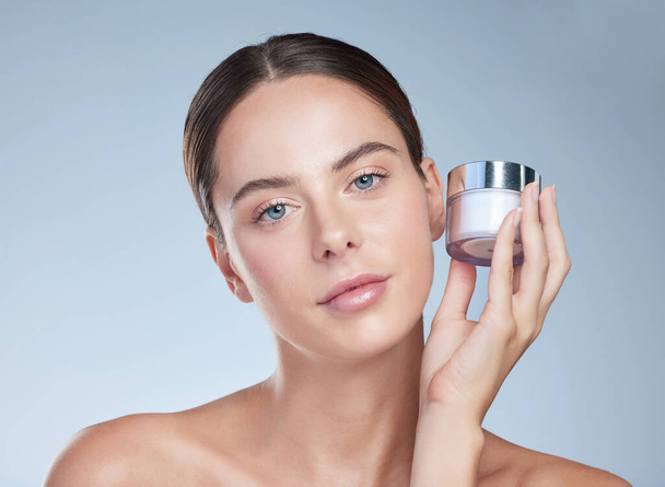The magic behind my incredible skin. Studio portrait of an attractive young woman posing with a container of moisturizer against a grey background - Фото, изображение