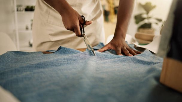 Creative designer cutting his fabric. Closeup of a tailor cutting denim material using a scissor. Fashion designer working in his studio. Entrepreneur cutting his textile on a table. - Φωτογραφία, εικόνα