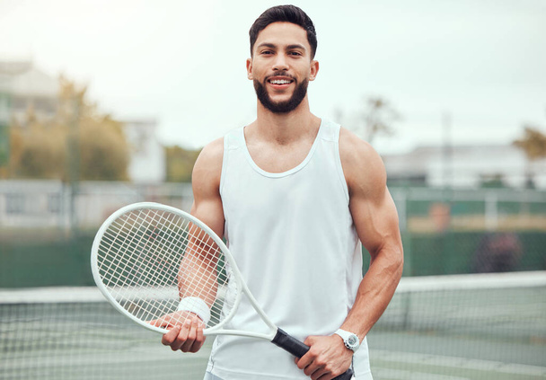 Portrait of smiling mixed race tennis player holding racket on court. Happy fit hispanic professional standing alone and feeling confident in sports club. Ready for an athletic match and healthy game. - Foto, Imagem