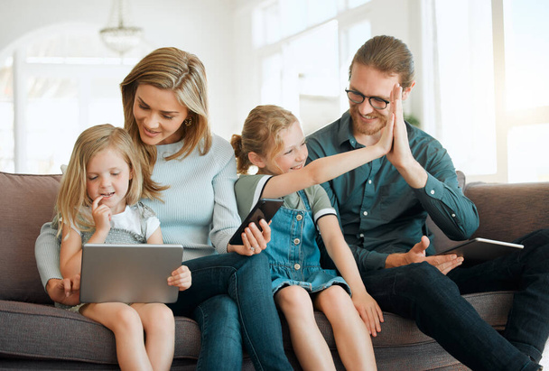 Мы все связаны по-своему. молодая семья, сидящая на диване вместе и соединяющаяся, используя технологию - Фото, изображение