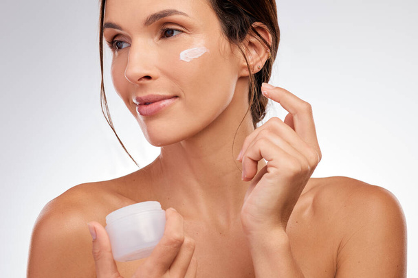 This creme is literally youth in a bottle. an attractive young woman applying moisturiser to her face in the studio - Foto, imagen