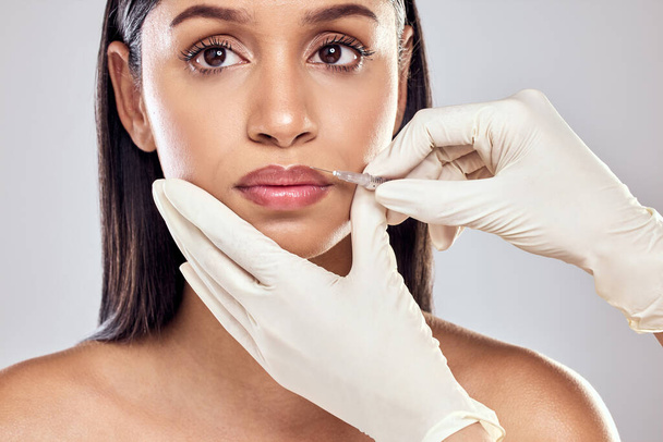 De dokter kan u nu ontvangen. een vrouw met haar lippen ingespoten met filler tegen een studio achtergrond - Foto, afbeelding