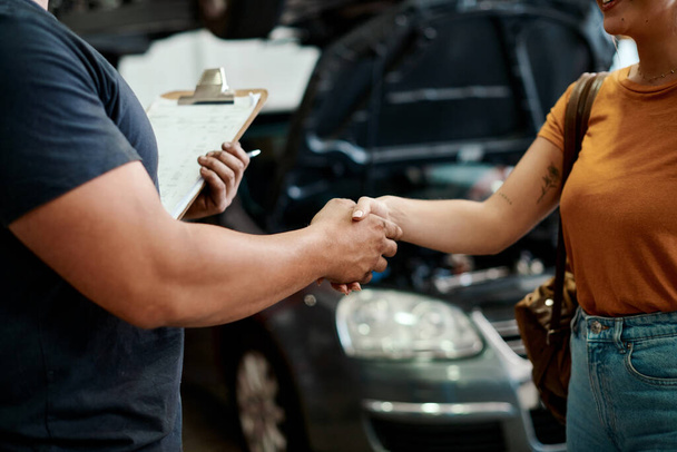 You can trust us to deliver on time. a woman shaking hands with a mechanic in an auto repair shop - Photo, Image