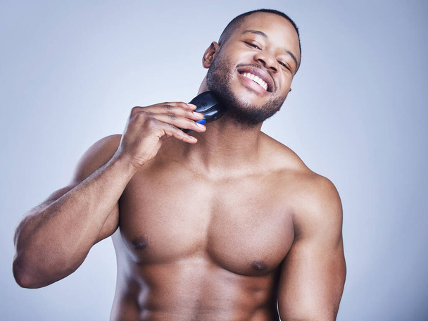 My secret weapon to looking my best. Studio shot of a handsome young man shaving his facial hair with an electrical razor against a blue background - Foto, afbeelding