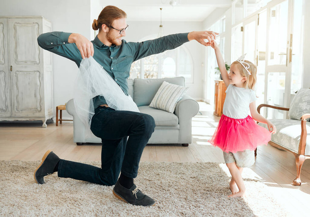 О, мне нужно подержать юбку. Полнометражный снимок очаровательной маленькой девочки в пачке и танцующей со своим отцом в гостиной - Фото, изображение