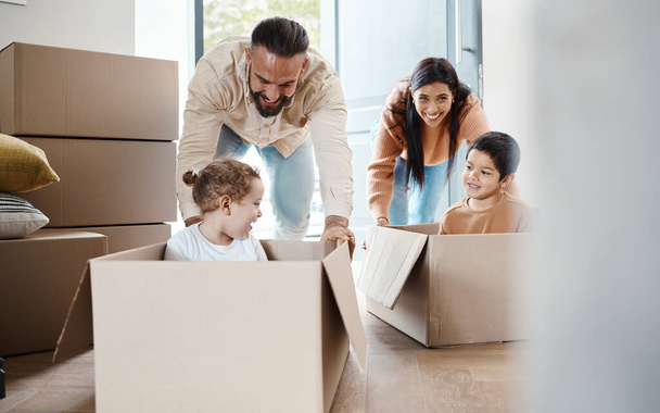 Playful, fun and a family moving into a house, bonding and unpacking their new home together. Happy, game and young parents pushing their children in a box, playing and relocation to an apartment. - Фото, зображення