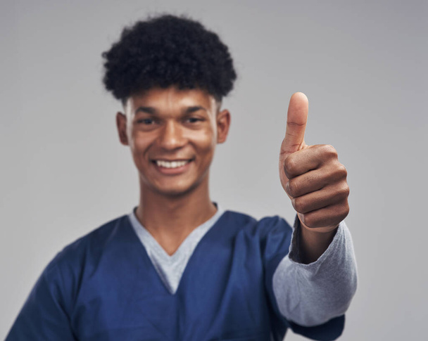 Ive made a lifelong commitment to help anyone and everyone. a male nurse showing thumbs up while standing against a grey background - Фото, изображение