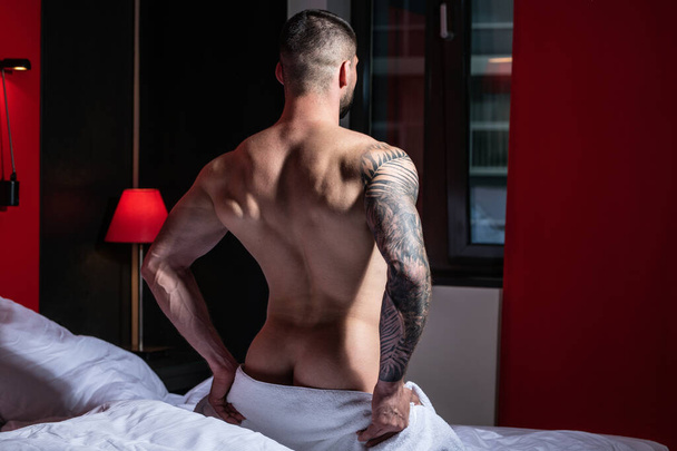 Handsome muscular man lying shirtless in bed. Young handsome man resting on the bed at home. Guy with thletic flexing muscles. Sexy young handsome naked man on bed. Seductive gay - Fotografie, Obrázek